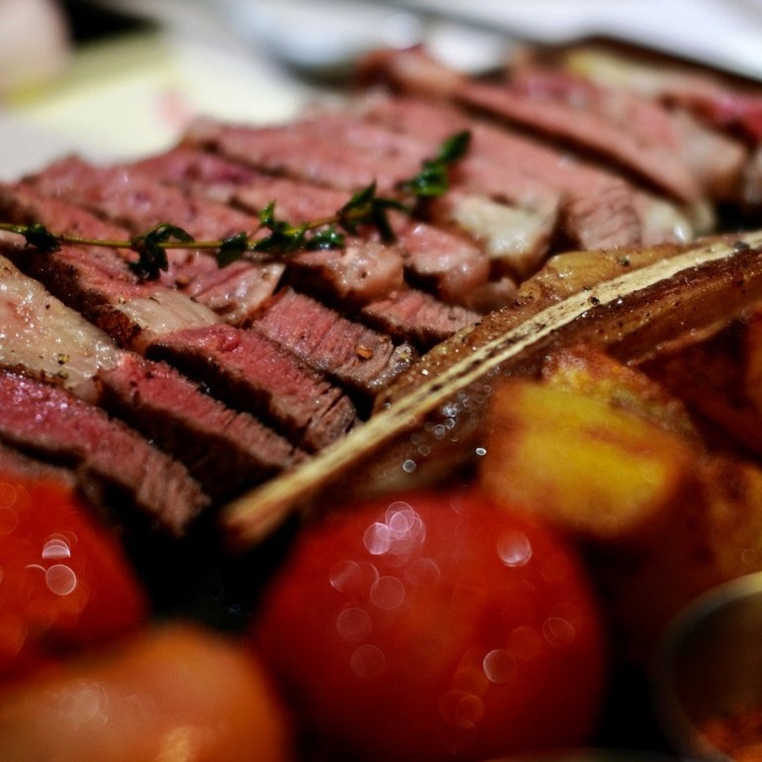 Sliced medium-rare steak with a thyme sprig, roasted cherry tomatoes and a charred potato wedge.
