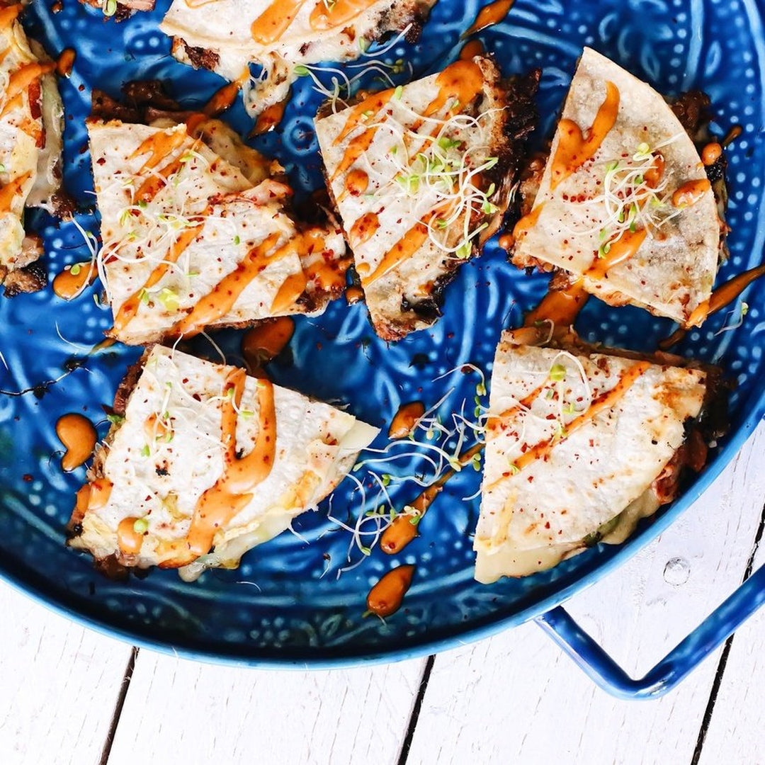 Chipotle steak quesadilla wedges on a patterned blue plate with orange sauce drizzle and microgreens