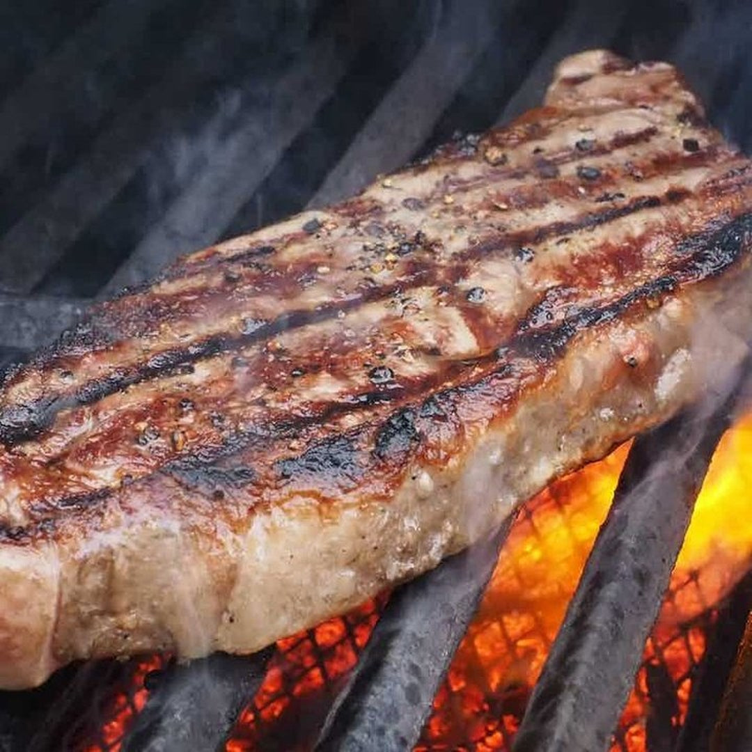 Grilled ribeye steak with charred grill marks over hot coals and orange flames