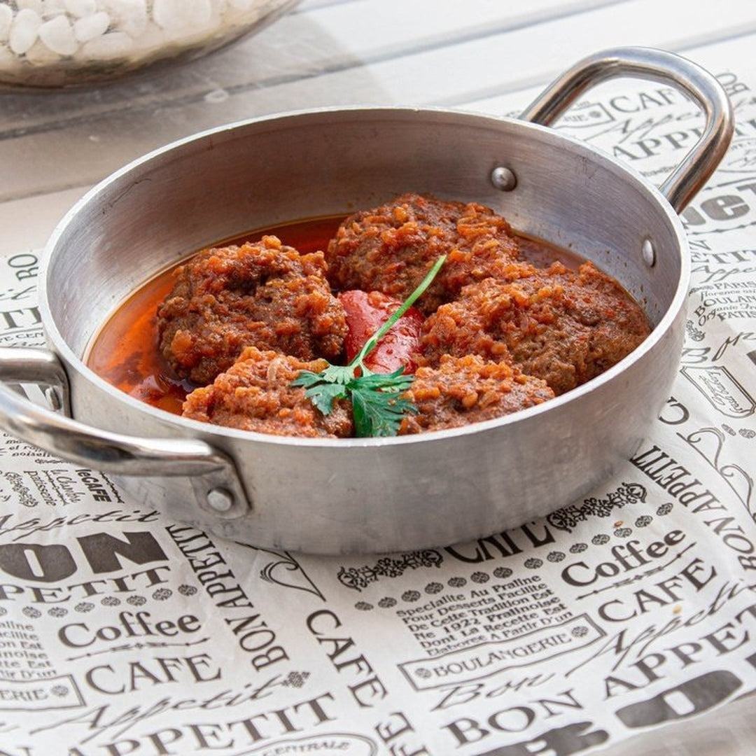 Meatballs in tomato sauce garnished with parsley in a metal pan on paper printed with 'Coffee', 'CAFE', 'BON APPETIT', 'BOULANGERIE'