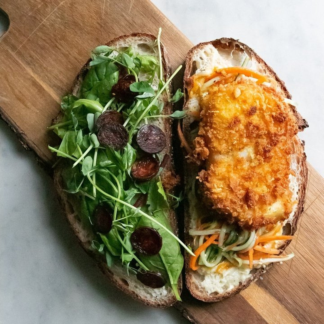 Open-faced chicken cutlet sandwich on rustic bread with crispy panko crust, pickled julienne vegetables and leafy greens