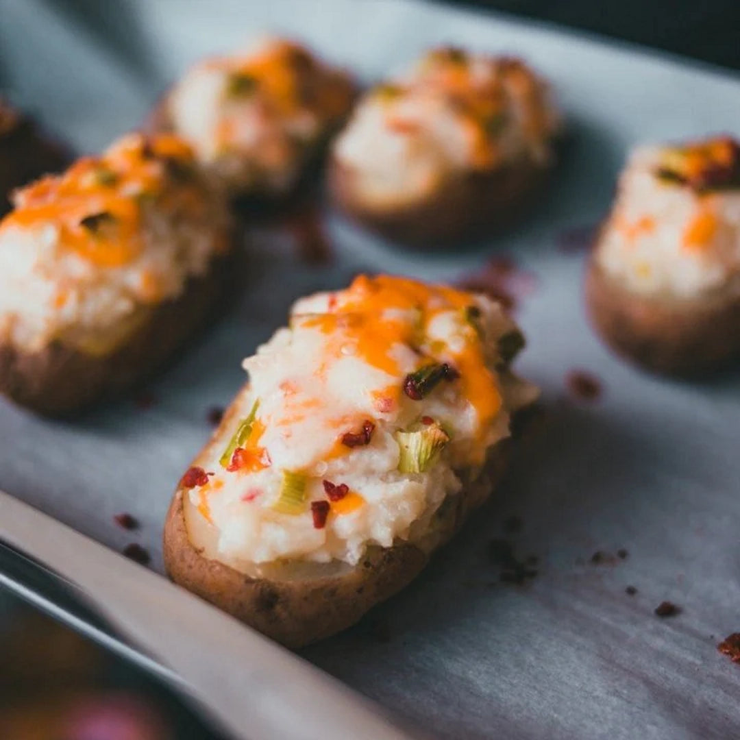 Twice-baked potato halves topped with lobster, melted cheddar, scallions, and red pepper flakes on a baking sheet