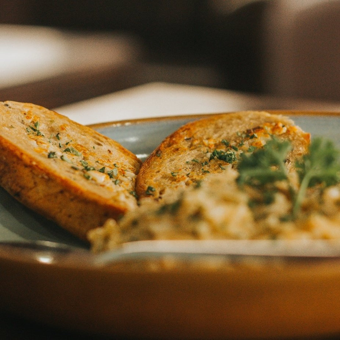 Two slices of roasted garlic and herb buttered bread on a blue plate, garnished with chopped parsley.