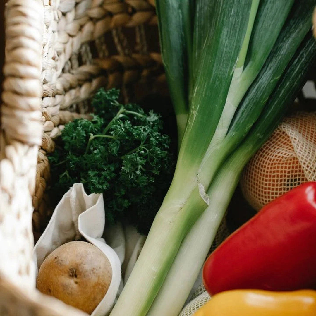 Fresh vegetables in a woven basket: leeks, curly parsley, a potato, and red and yellow bell peppers