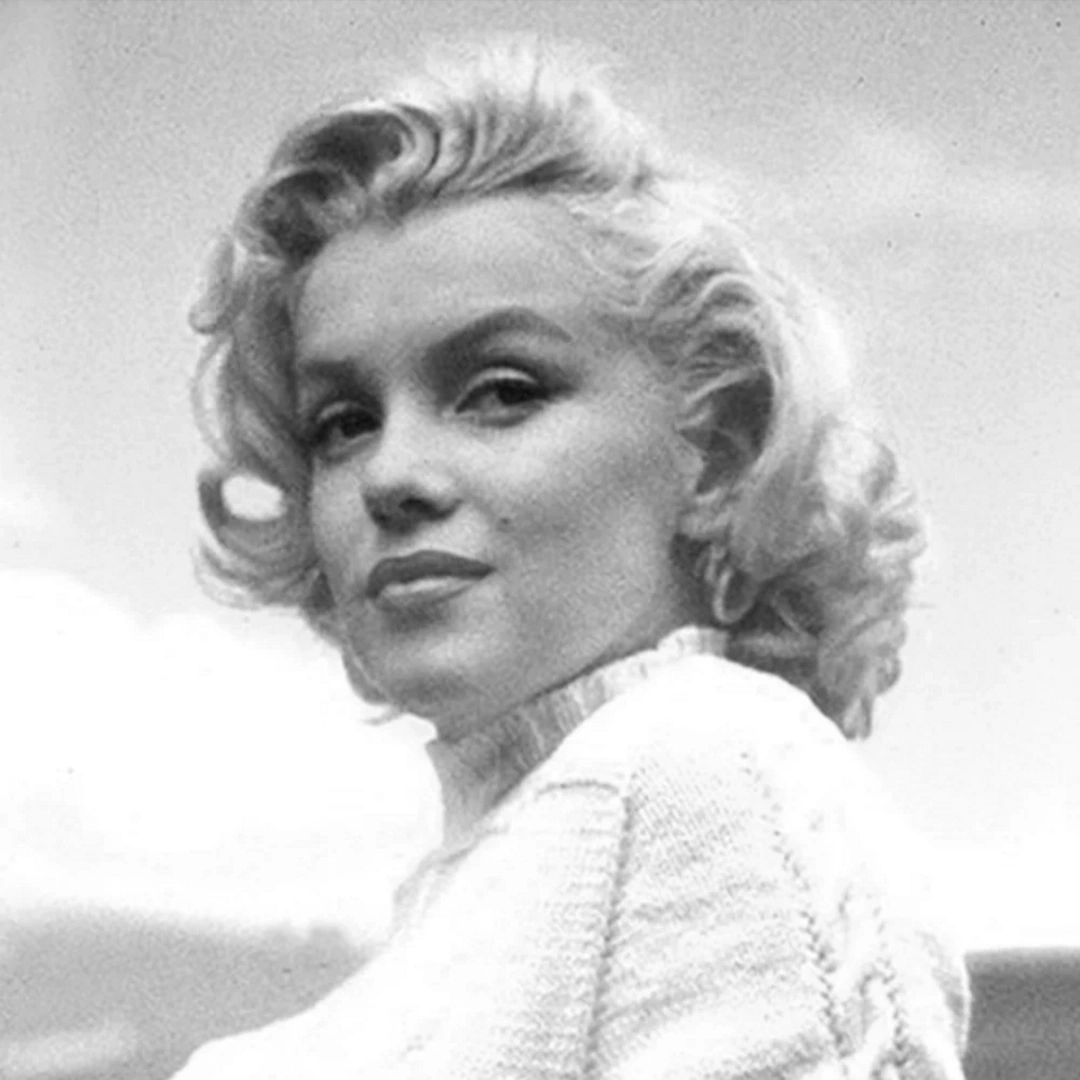Black-and-white portrait of Marilyn Monroe in a knit sweater, looking over her shoulder with short curled hair.