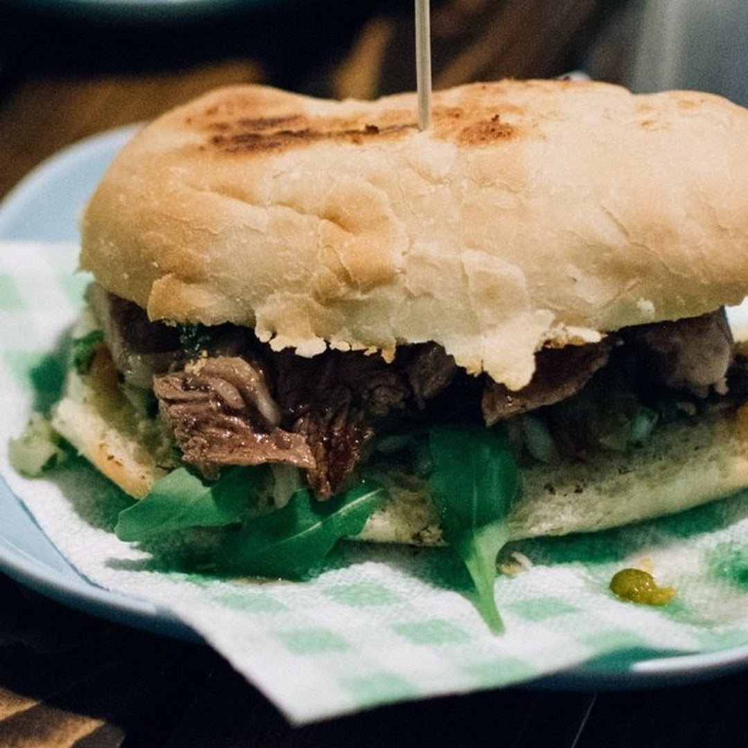 Slow-cooked French dip sandwich on toasted roll with shredded beef, arugula and toothpick, on green-checkered napkin