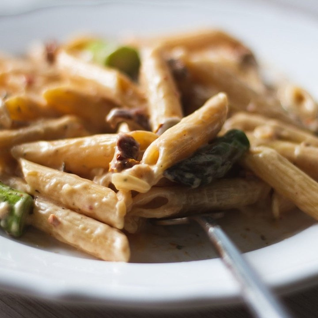 Creamy penne pasta with asparagusin a French onion-style sauce on a white plate with a fork.