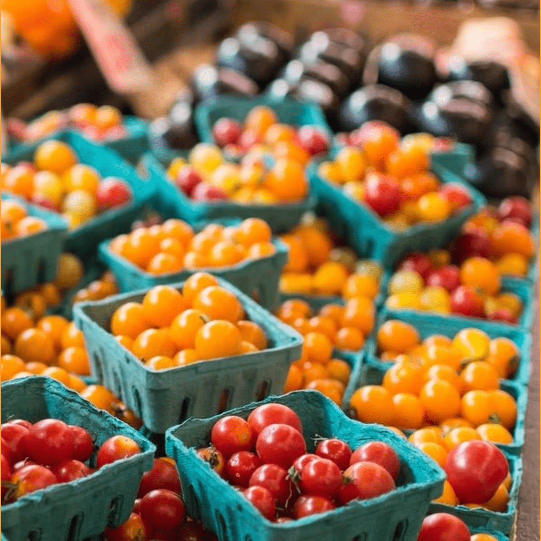 Green pint baskets filled with red, orange, and yellow cherry tomatoes at a farmers' market