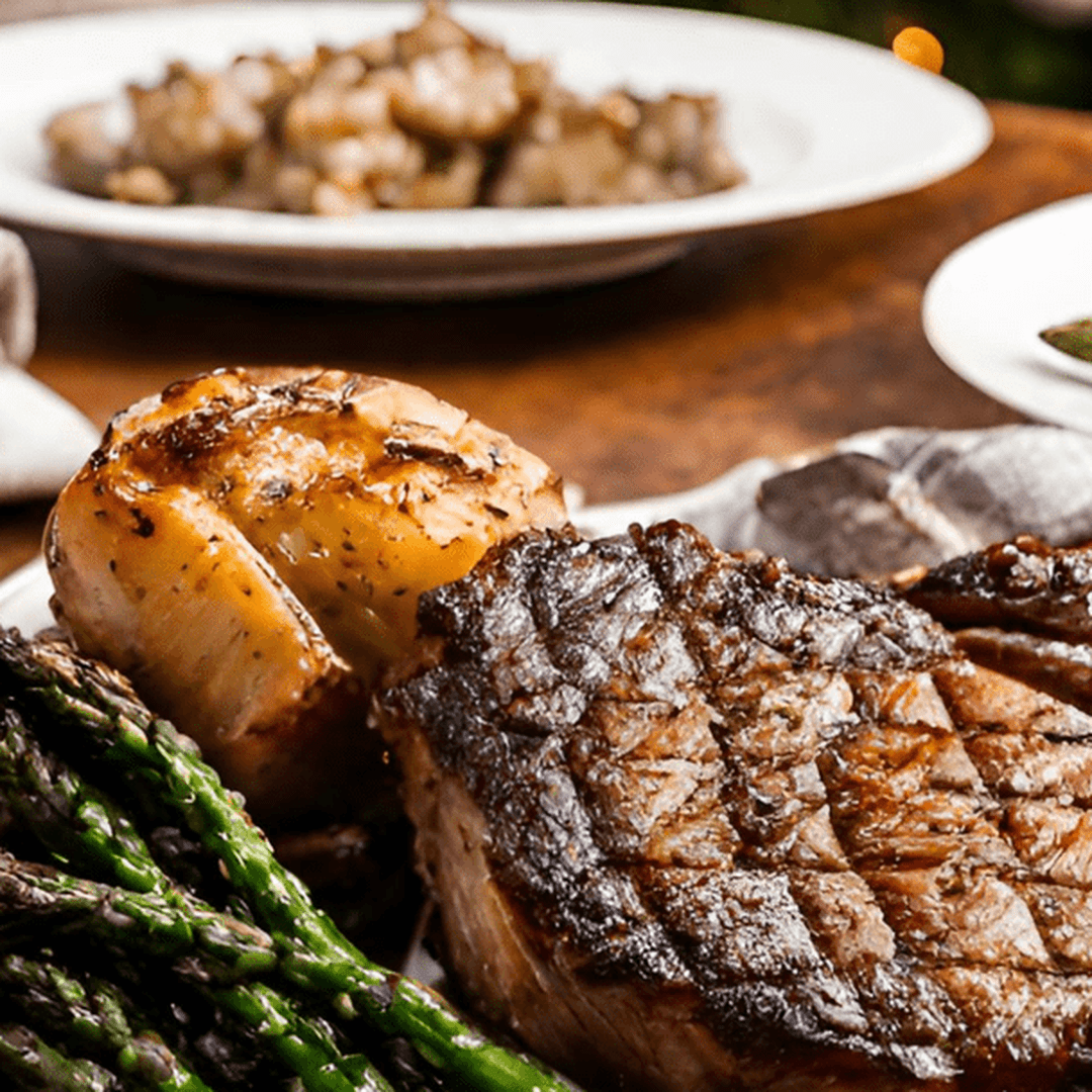 Grilled ribeye steak with roasted garlic potato and asparagus on a wooden table