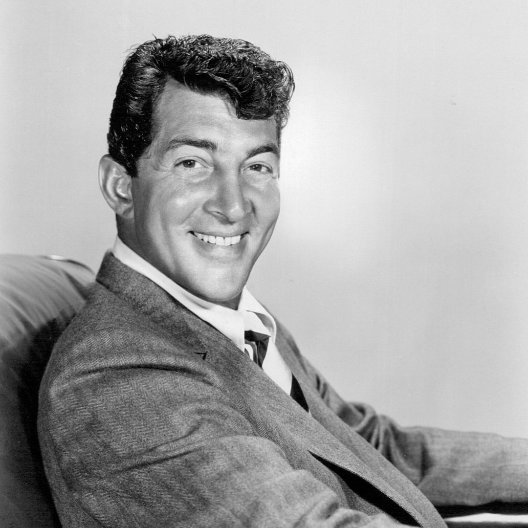 Vintage black-and-white studio portrait of Dean Martin in a suit, seated in three-quarter view.