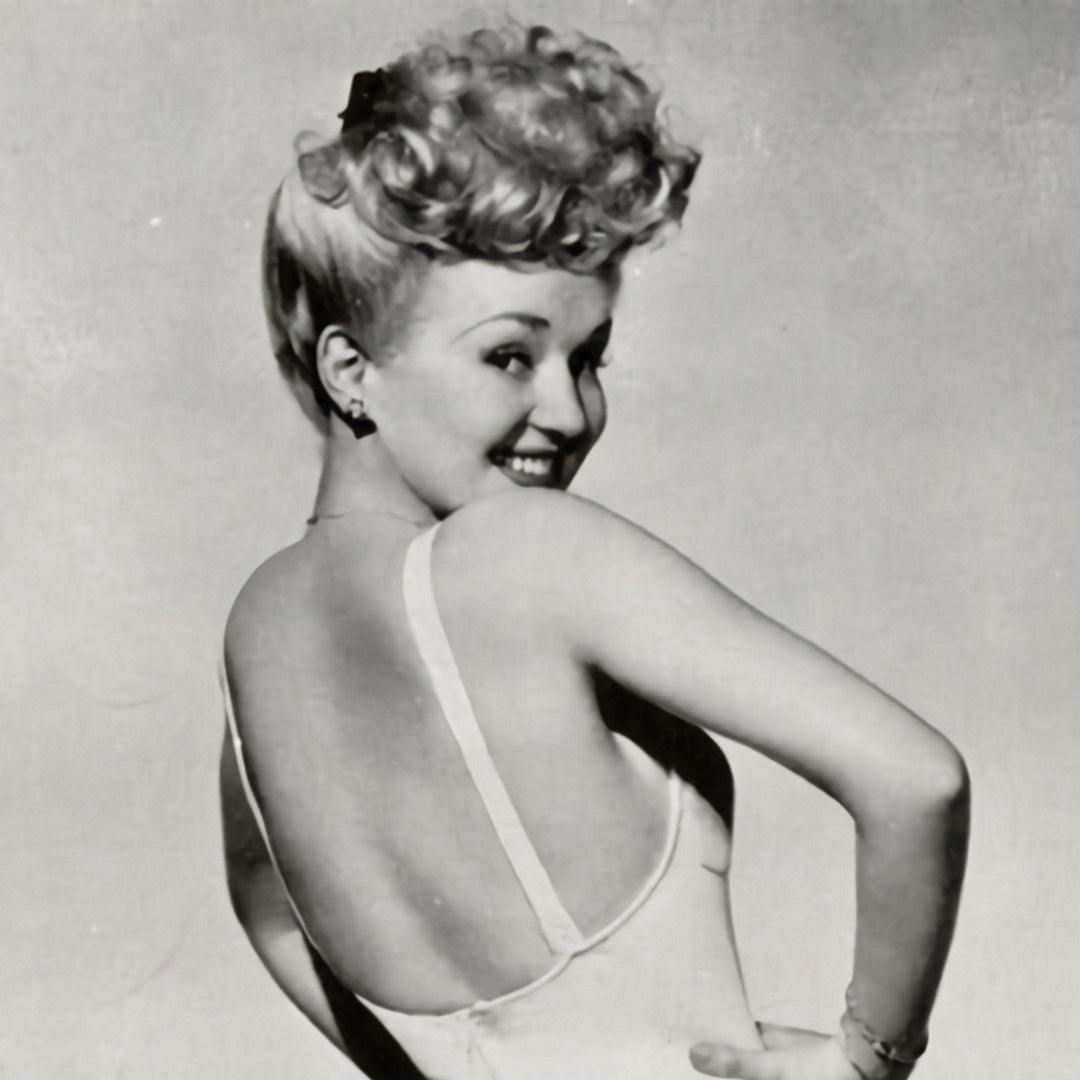 Betty Grable in a vintage pin-up pose, looking over her shoulder in a low-back dress with curled 1940s hairstyle.
