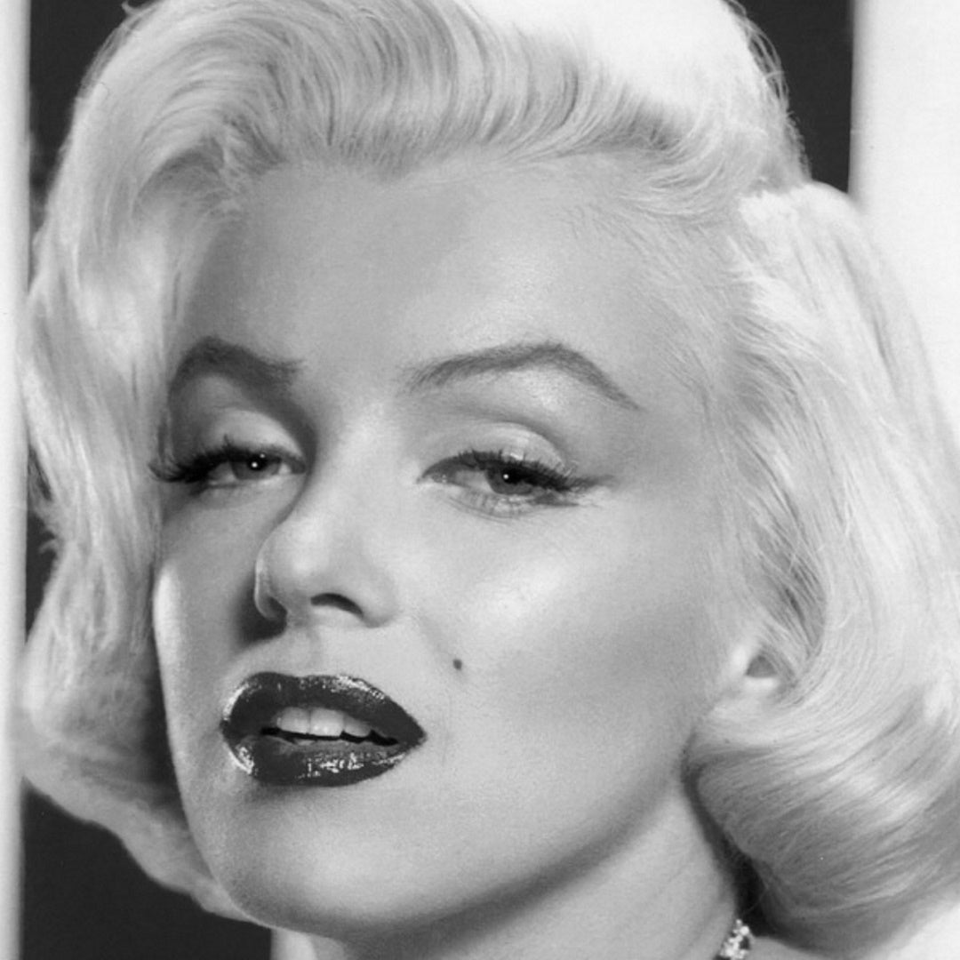 Black-and-white close-up portrait of Marilyn Monroe with short wavy hair, beauty mark, and glossy dark lipstick.