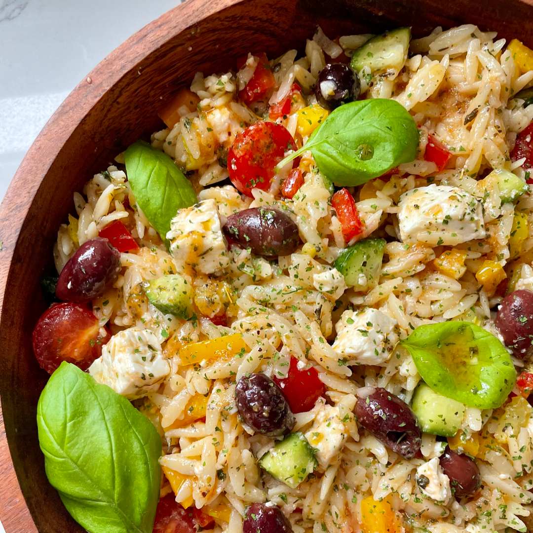 Mediterranean orzo salad with feta cubes, kalamata olives, cherry tomatoes, cucumber, bell pepper and basil in wooden bowl