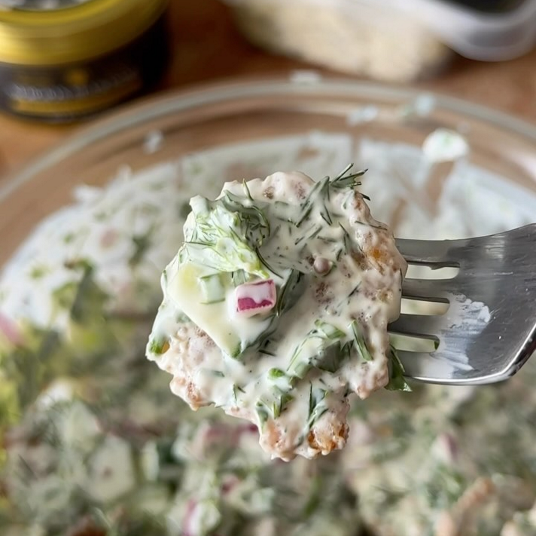Forkful of creamy potato salad with dill, chopped radish and cucumber over a glass bowl