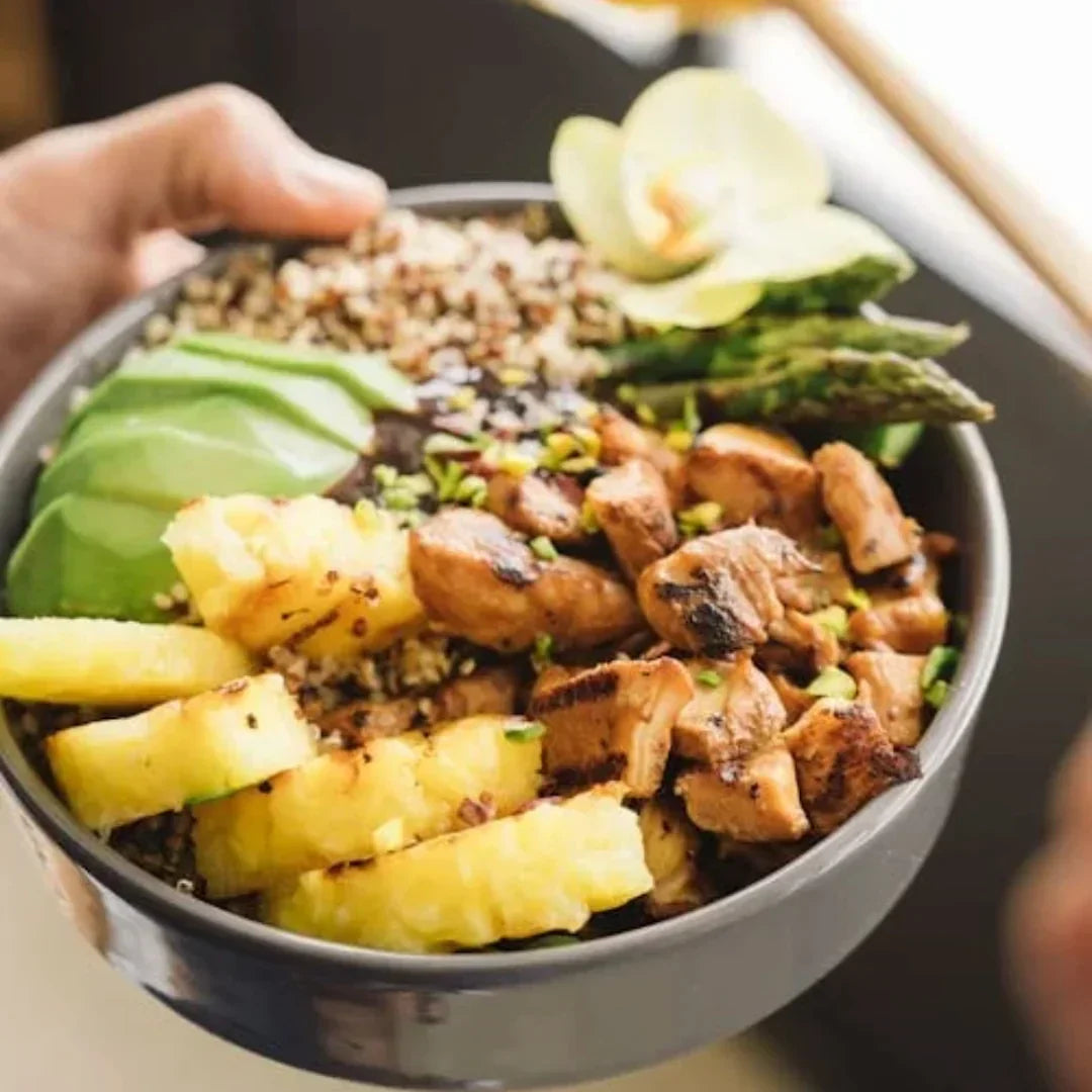Bowl with grilled chicken, pineapple slices, avocado, quinoa, asparagus and edible orchid garnish