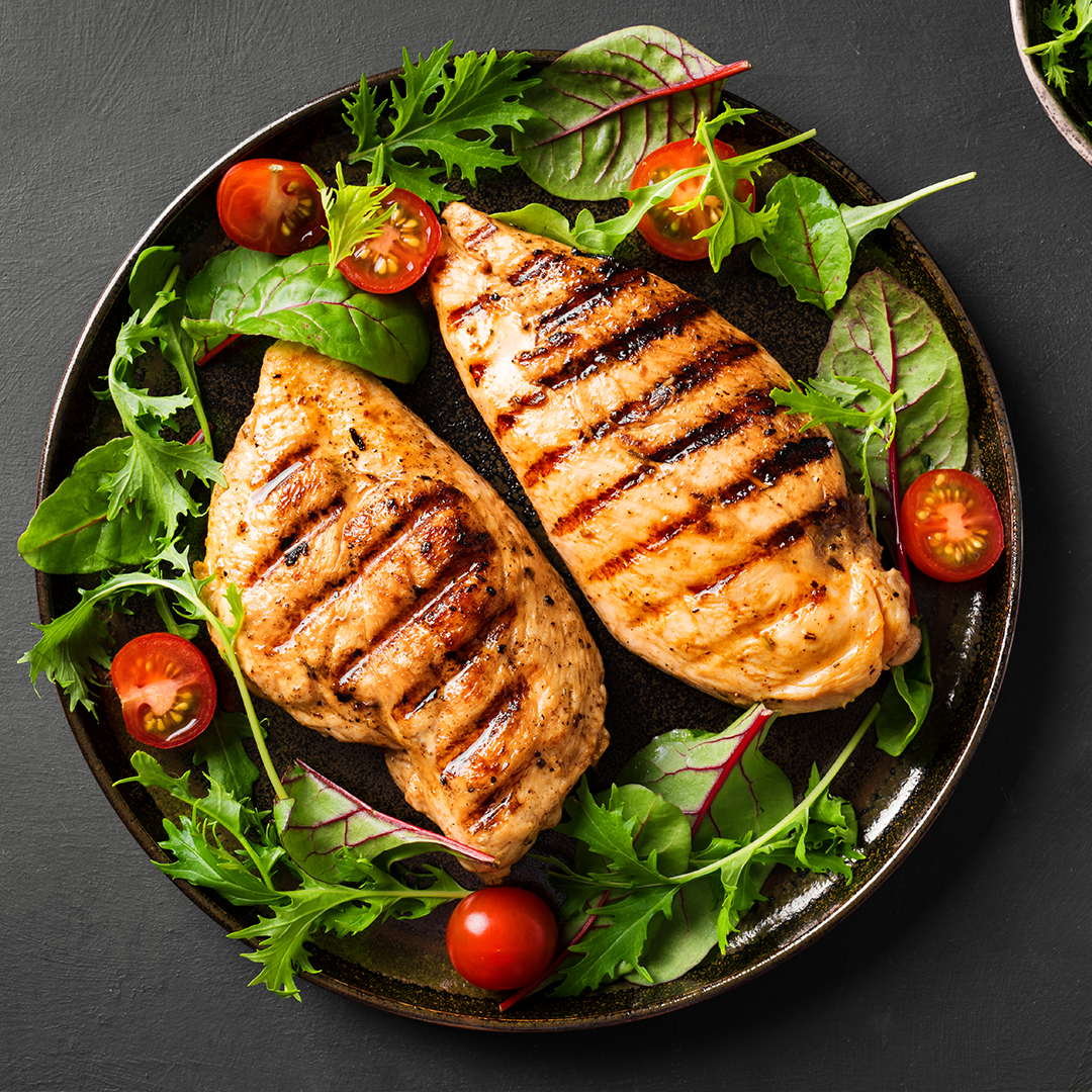 Grilled lemon-pepper chicken breasts with mixed greens and cherry tomatoes on a round dark plate
