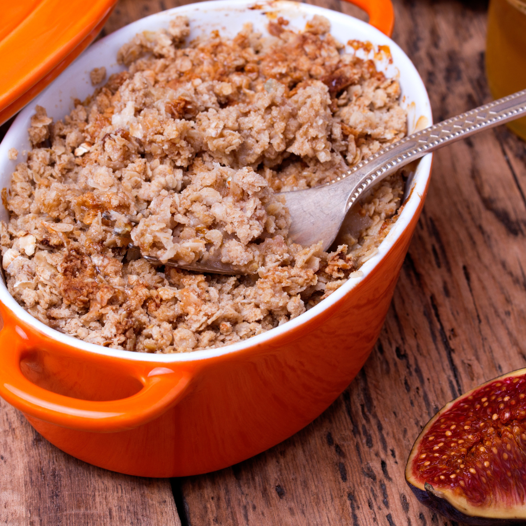 Top view of apple and fig crisp showcasing its crumbly topping in an orange baking dish with a spoon on a wooden table