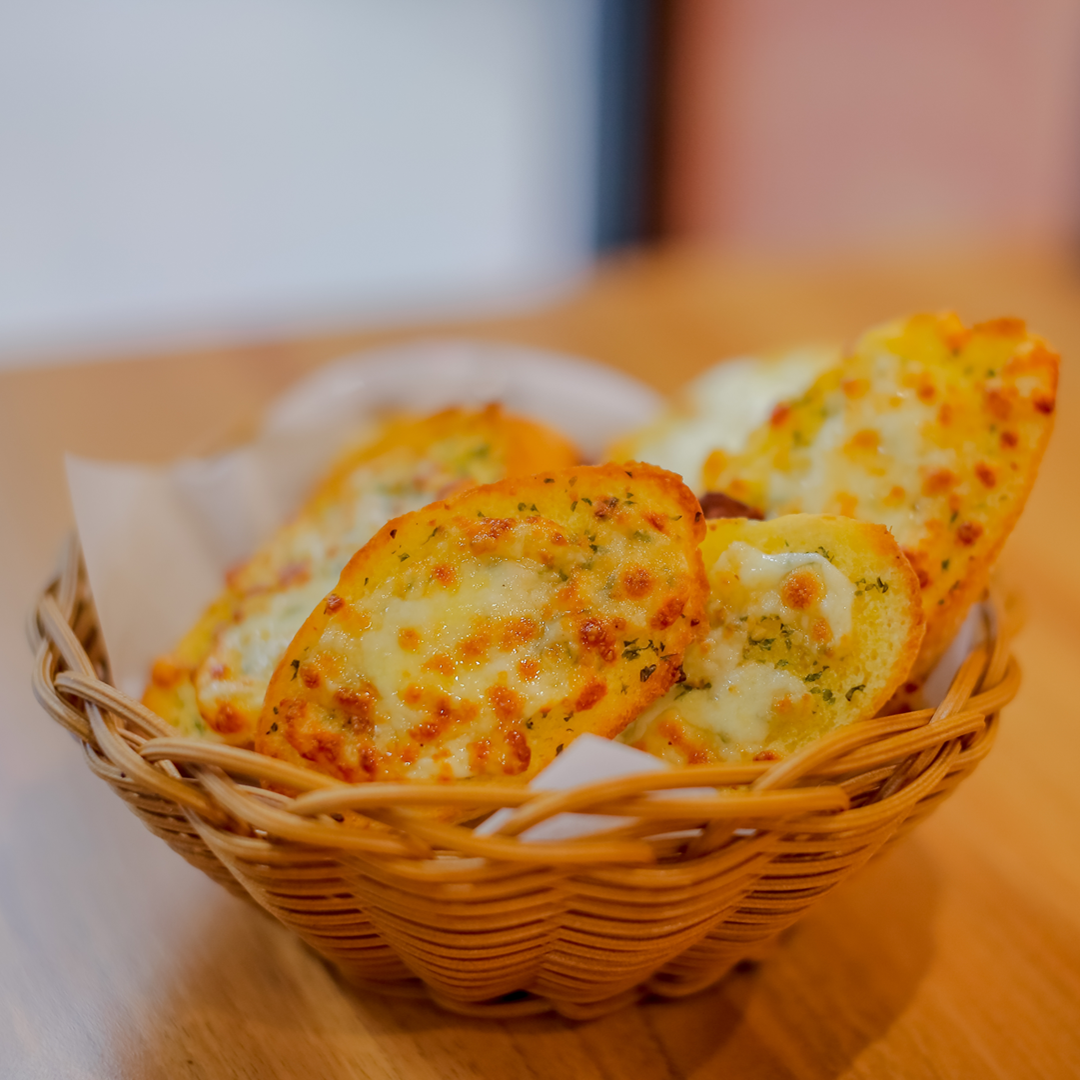 Close-up of steakhouse garlic bread topped with melted cheese and herbs in a woven basket