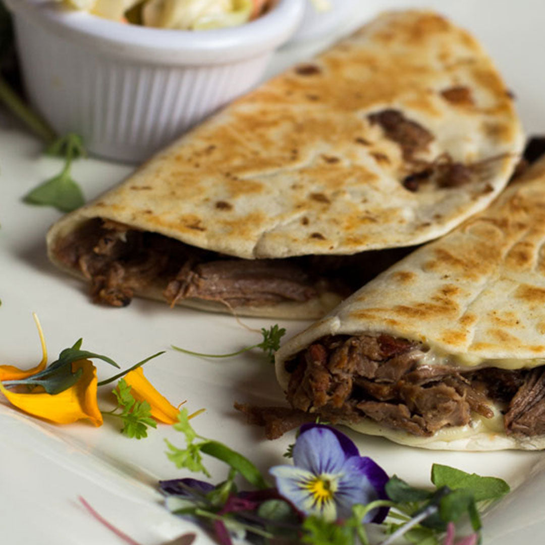 Crockpot brisket tacos with shredded beef and melted cheese in warm flour tortillas, garnished with herbs and edible flowers.