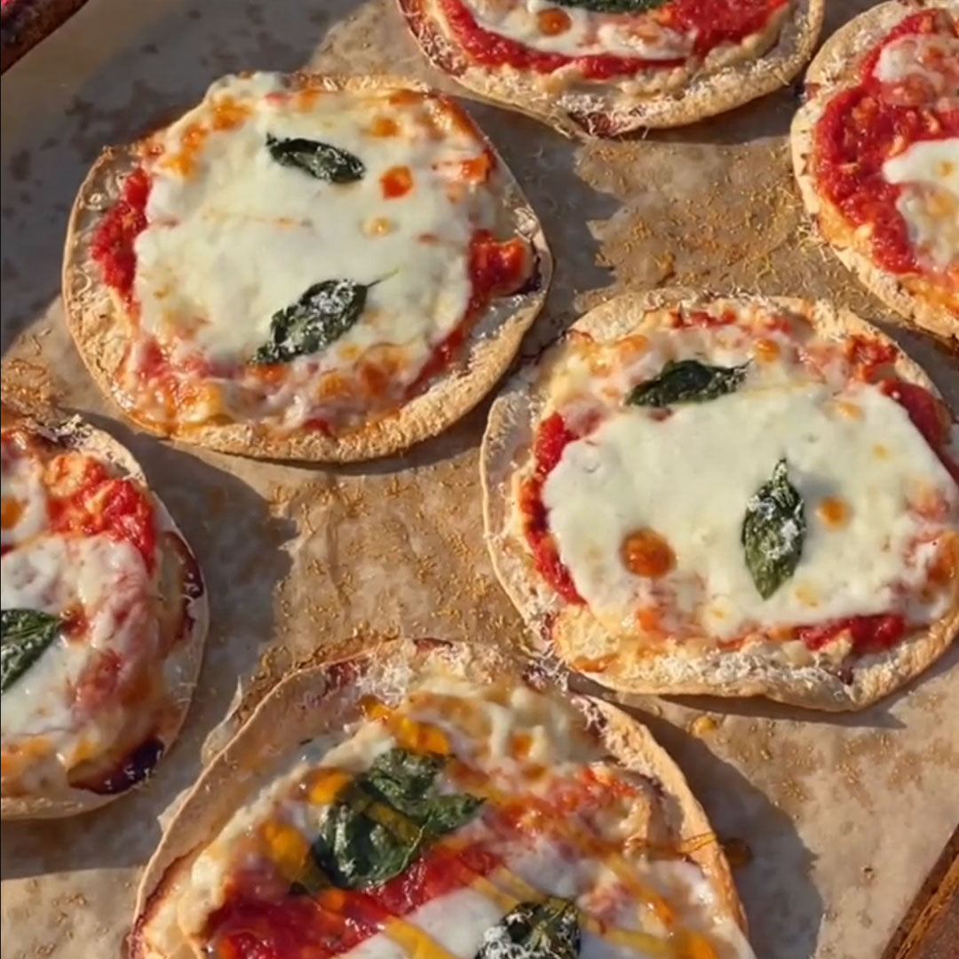 Round tacos topped with tomato sauce melted mozzarella and fresh basil on a sheet pan