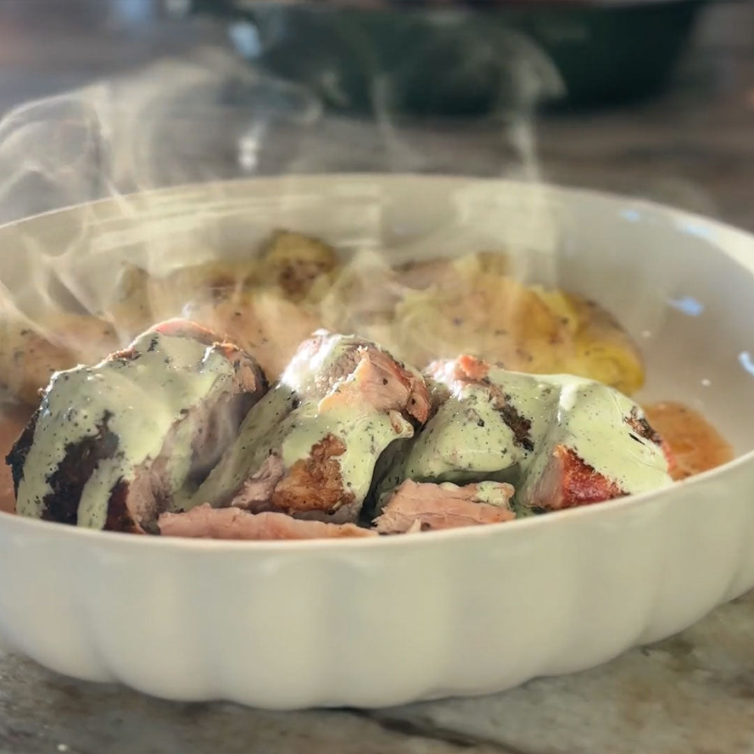 Sliced grilled pork loin with creamy green herb sauce on a white baking dish