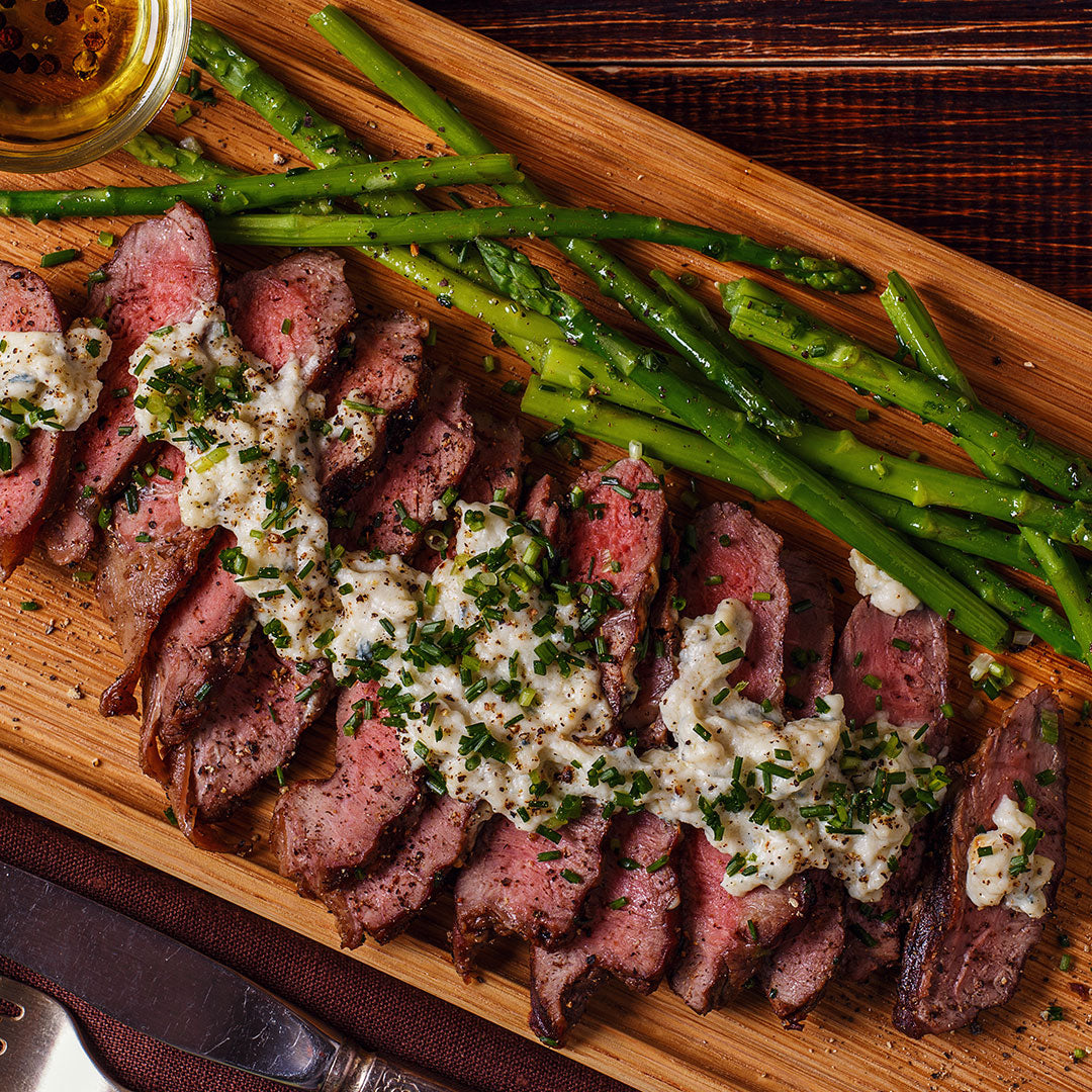 Sliced spring steak topped with herb butter and roasted asparagus arranged on a wooden board.