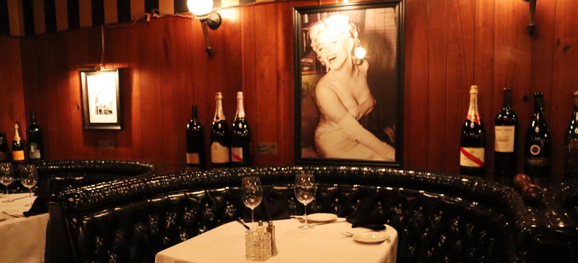 Dining area with black leather booths, white tablecloths, and wine bottles on a wooden wall.