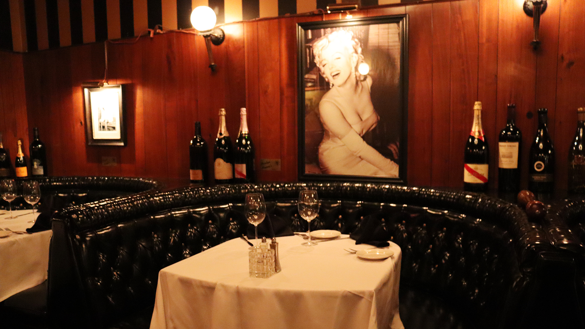 Dining area with tables, chairs, and wine bottles in a restaurant setting.