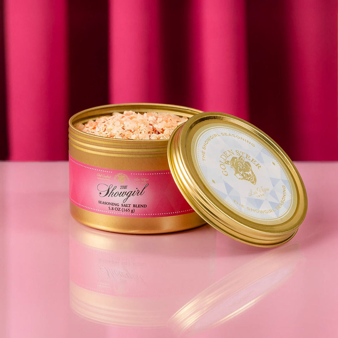 Open container of 'he Showgirl seasoning blend with pink label on a pink background